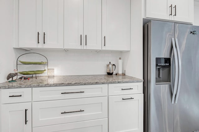 kitchen featuring stainless steel refrigerator with ice dispenser, light stone countertops, decorative backsplash, and white cabinets