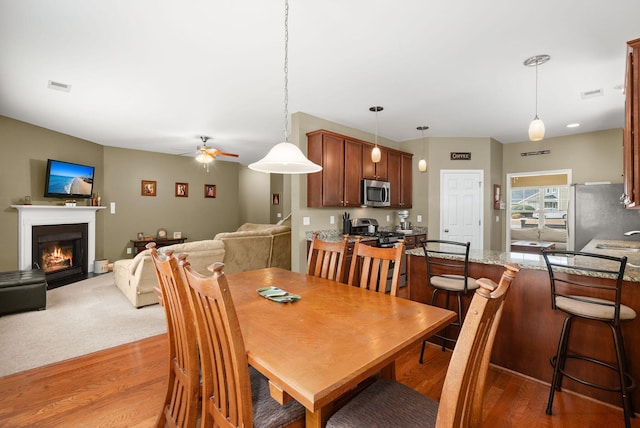 dining space featuring a fireplace with flush hearth, a ceiling fan, visible vents, and light wood finished floors