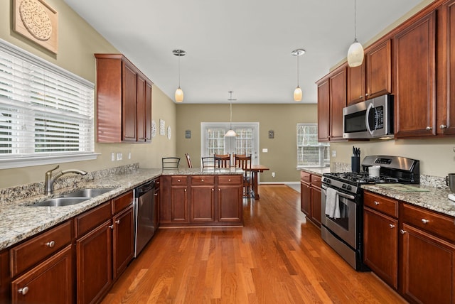 kitchen featuring decorative light fixtures, a peninsula, wood finished floors, stainless steel appliances, and a sink