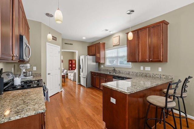 kitchen featuring a kitchen bar, light wood-style flooring, light stone counters, appliances with stainless steel finishes, and a peninsula