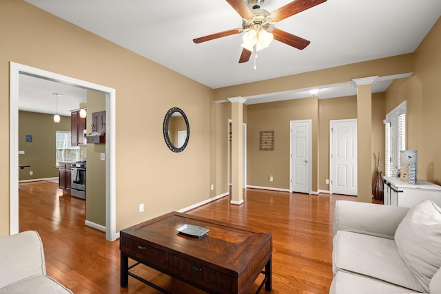 living room with light wood finished floors, ceiling fan, baseboards, and ornate columns