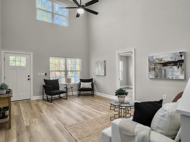 living room with ceiling fan, a towering ceiling, and light hardwood / wood-style flooring