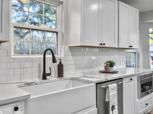 kitchen with sink, white cabinetry, light stone counters, stainless steel appliances, and backsplash