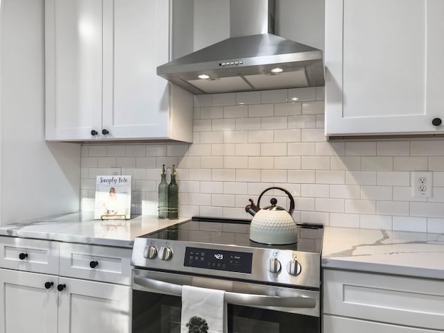 kitchen with tasteful backsplash, light stone counters, wall chimney range hood, stainless steel electric stove, and white cabinets