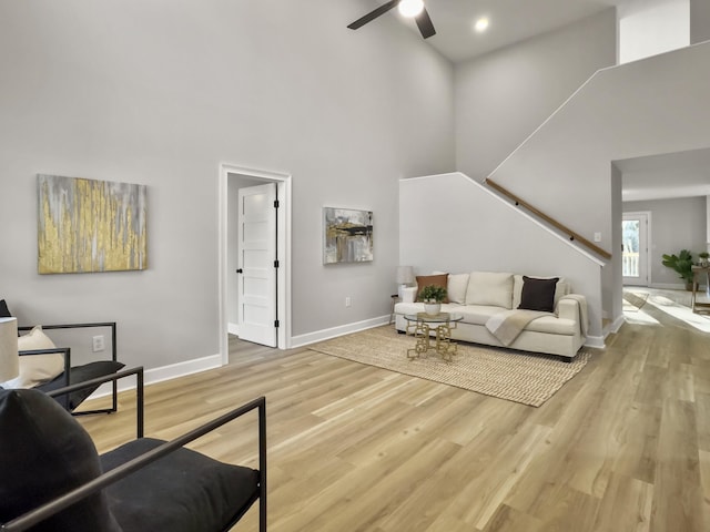 living room featuring a towering ceiling, ceiling fan, and light wood-type flooring