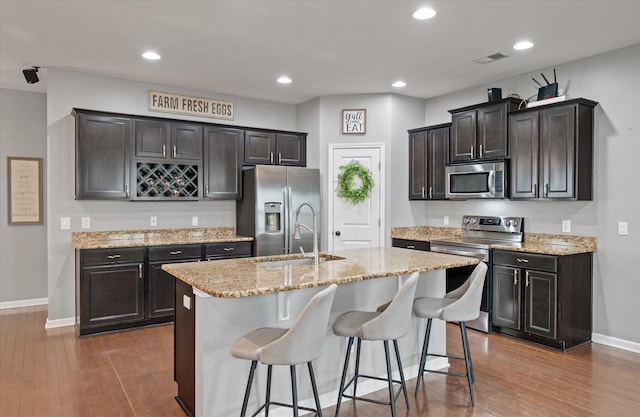 kitchen featuring a kitchen bar, dark brown cabinets, dark hardwood / wood-style floors, an island with sink, and stainless steel appliances