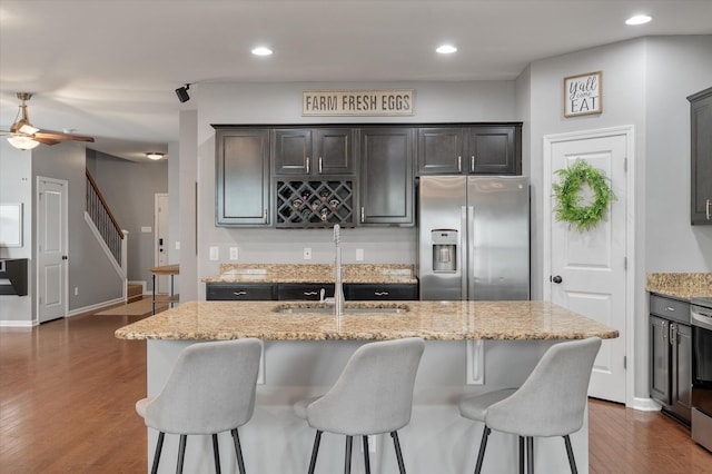 kitchen featuring dark wood-type flooring, sink, light stone counters, stainless steel appliances, and a kitchen island with sink