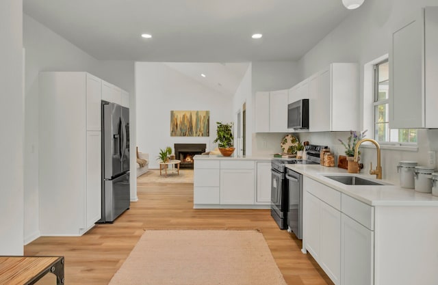 kitchen with stainless steel appliances, sink, vaulted ceiling, white cabinets, and light hardwood / wood-style flooring