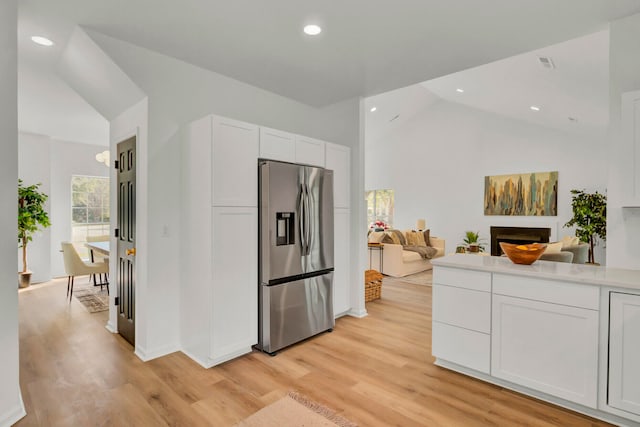 kitchen with stainless steel refrigerator with ice dispenser, white cabinetry, light wood-type flooring, and lofted ceiling