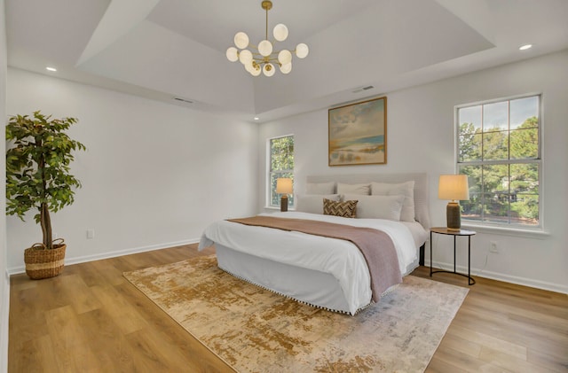 bedroom with light hardwood / wood-style floors, multiple windows, and a raised ceiling