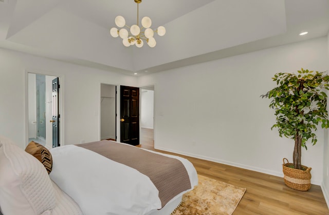 bedroom featuring ensuite bath, a chandelier, a tray ceiling, and light hardwood / wood-style flooring