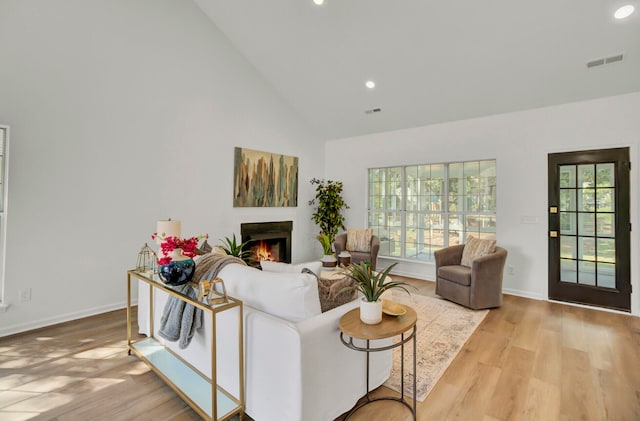 living room featuring a healthy amount of sunlight, light wood-type flooring, and high vaulted ceiling