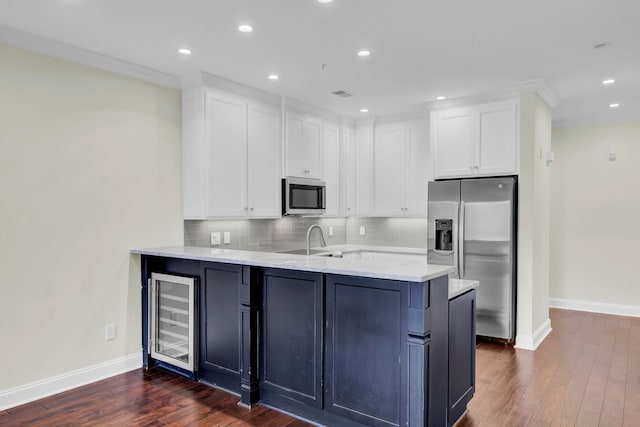 kitchen with kitchen peninsula, appliances with stainless steel finishes, beverage cooler, dark wood-type flooring, and white cabinetry