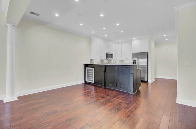 kitchen featuring dark wood-type flooring, stainless steel appliances, wine cooler, decorative columns, and white cabinets