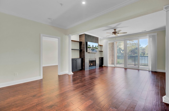 unfurnished living room featuring ornamental molding, a fireplace, dark wood-type flooring, ceiling fan, and decorative columns