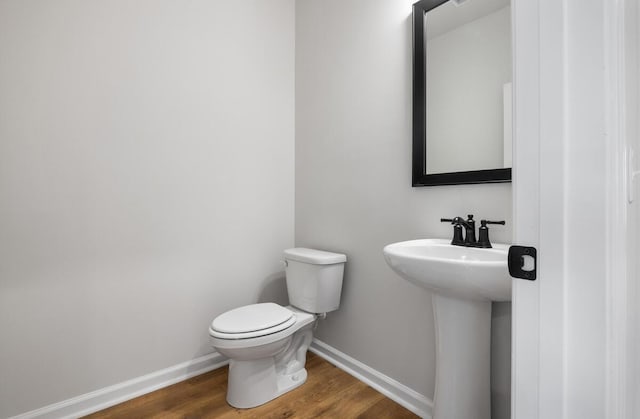 half bath with a sink, baseboards, toilet, and wood finished floors