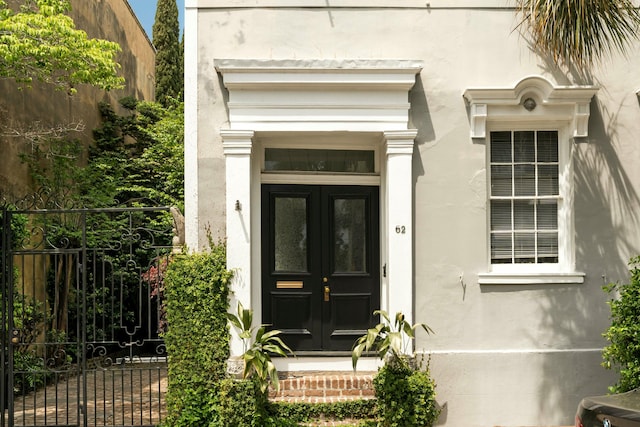 view of exterior entry with french doors, fence, stucco siding, and a gate