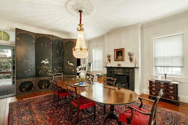 dining space with a premium fireplace, ornamental molding, hardwood / wood-style flooring, and a notable chandelier
