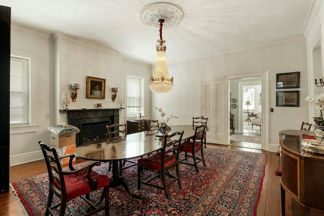 dining area featuring ornamental molding, a fireplace, wood finished floors, and a notable chandelier