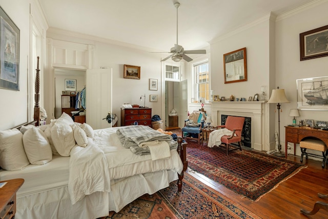 bedroom featuring ceiling fan, ornamental molding, wood finished floors, and a fireplace