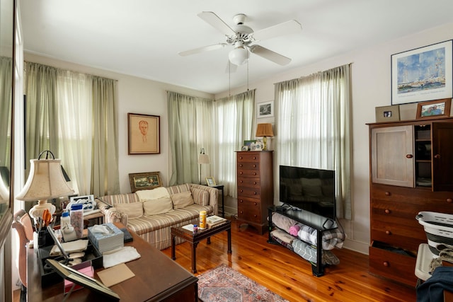 living area with baseboards, ceiling fan, and wood finished floors