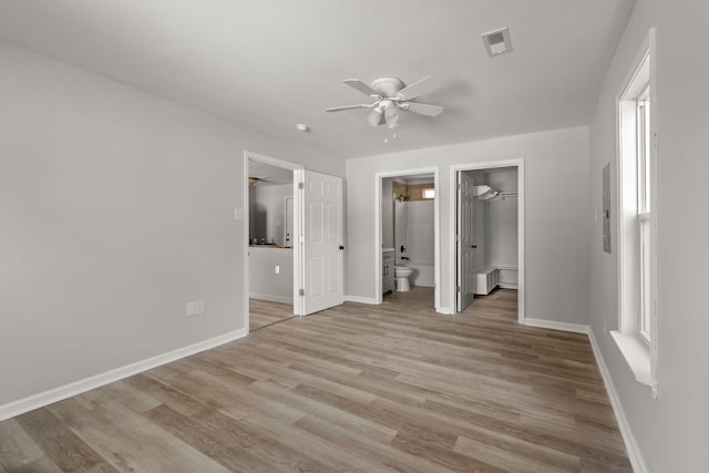 unfurnished bedroom featuring connected bathroom, light hardwood / wood-style flooring, a closet, ceiling fan, and a spacious closet