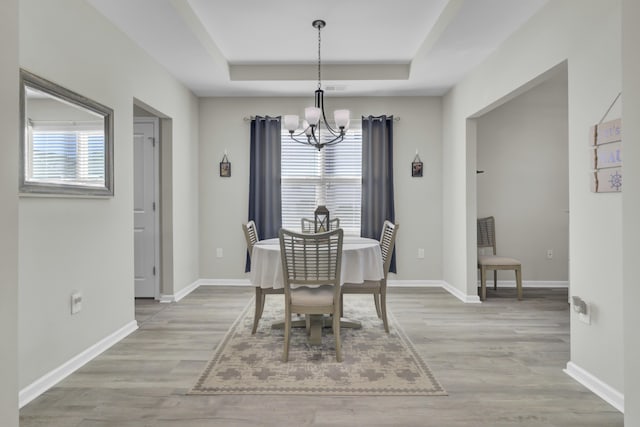 dining space with a raised ceiling, a healthy amount of sunlight, light hardwood / wood-style flooring, and a chandelier