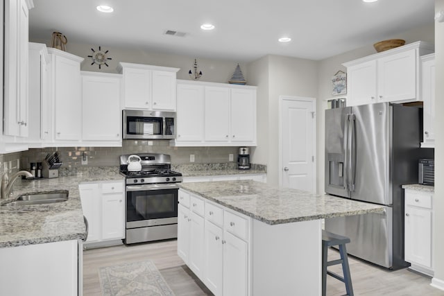 kitchen with appliances with stainless steel finishes, sink, light hardwood / wood-style flooring, white cabinets, and a kitchen island