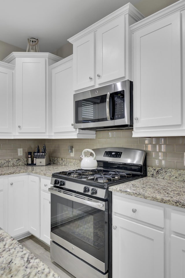 kitchen with white cabinets, appliances with stainless steel finishes, backsplash, and light stone countertops