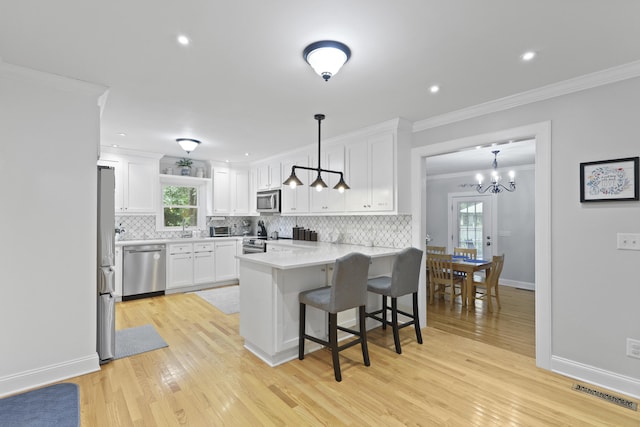 189 Fox Chase Dr, Goose Creek, SC 29445 - kitchen with stainless steel appliances, a peninsula, ornamental molding, white cabinets, and light wood finished floors