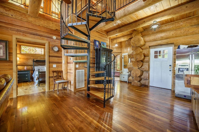 staircase featuring hardwood / wood-style flooring, rustic walls, beam ceiling, a high ceiling, and wooden ceiling