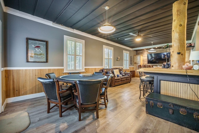 dining area featuring wainscoting, ornamental molding, wood ceiling, wood finished floors, and wood walls