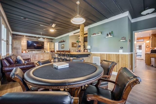 dining area featuring wooden walls, a wainscoted wall, wood finished floors, crown molding, and wooden ceiling