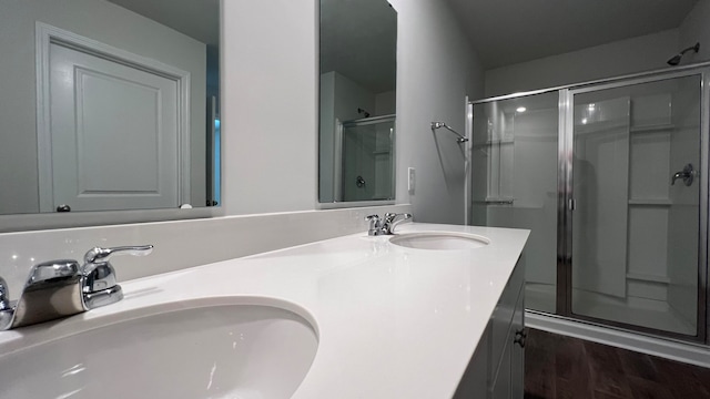 bathroom featuring a shower with shower door, dual bowl vanity, and hardwood / wood-style flooring