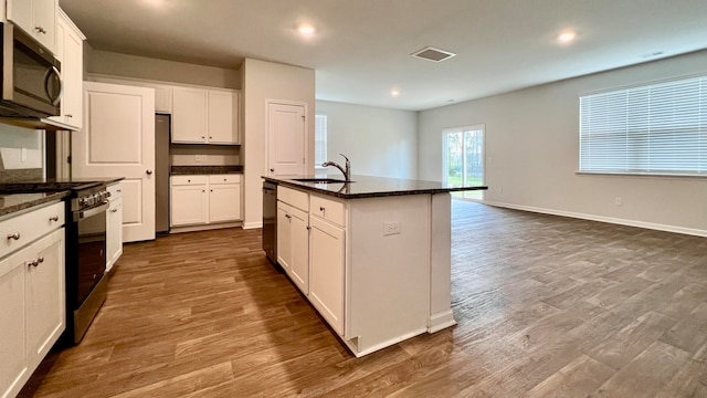 kitchen with a center island with sink, dark wood-type flooring, appliances with stainless steel finishes, white cabinets, and sink