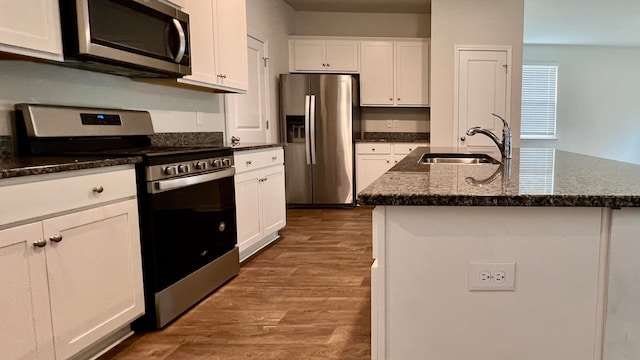 kitchen featuring appliances with stainless steel finishes, white cabinets, an island with sink, hardwood / wood-style floors, and sink