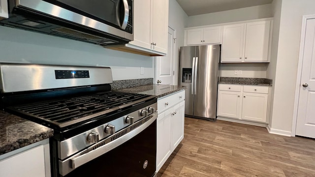 kitchen with appliances with stainless steel finishes, light hardwood / wood-style flooring, dark stone countertops, and white cabinets