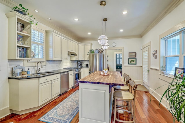 kitchen with a breakfast bar, stainless steel appliances, light wood-style floors, a sink, and under cabinet range hood