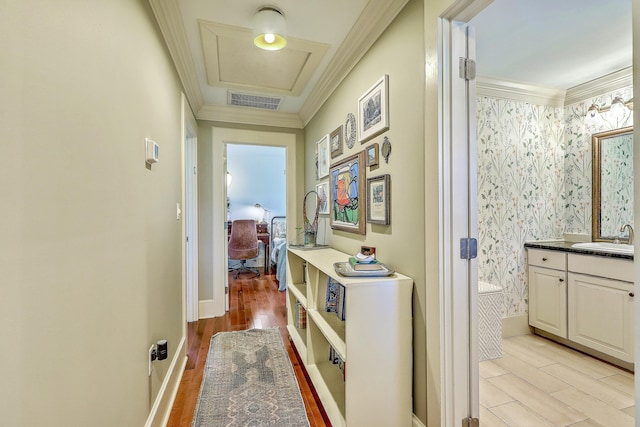 corridor with crown molding, light wood-type flooring, a sink, and wallpapered walls