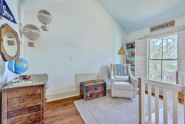 bedroom featuring lofted ceiling, a nursery area, baseboards, and wood finished floors