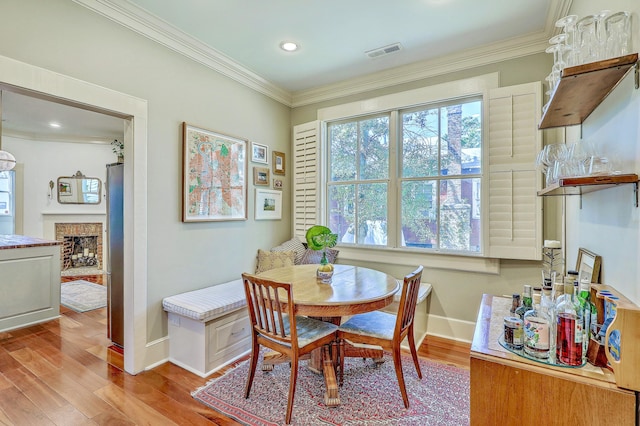 dining area featuring baseboards, visible vents, crown molding, light wood-type flooring, and a fireplace