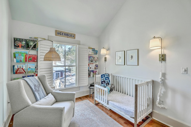 bedroom featuring lofted ceiling, baseboards, a nursery area, and wood finished floors