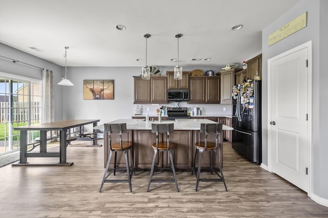 9009 Chato Ct, Summerville, SC 29483 - kitchen featuring appliances with stainless steel finishes, backsplash, light wood-style flooring, a center island with sink, and light countertops