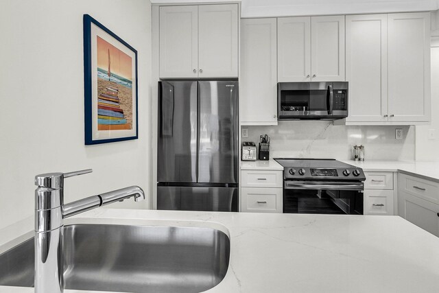 kitchen with appliances with stainless steel finishes, decorative backsplash, sink, and white cabinets