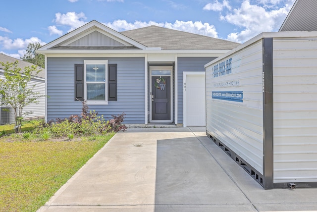 property entrance with central AC unit, roof with shingles, and a lawn