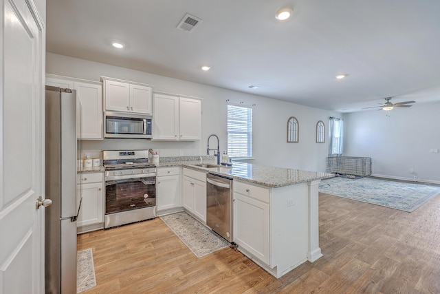 kitchen with stainless steel appliances, a peninsula, white cabinetry, light wood-style flooring, and a sink