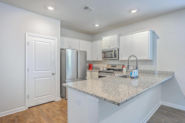 kitchen featuring stainless steel appliances, a sink, a peninsula, white cabinets, and light stone counters