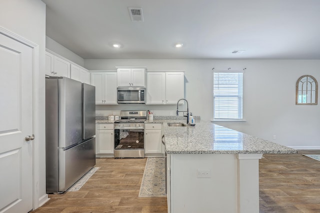 kitchen with appliances with stainless steel finishes, a sink, a peninsula, light wood-style flooring, and white cabinetry