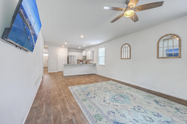 unfurnished living room with wood finished floors, a ceiling fan, baseboards, and recessed lighting