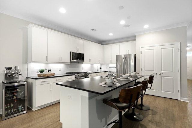 kitchen with stainless steel appliances, wine cooler, a breakfast bar area, ornamental molding, and wood finished floors